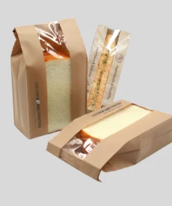 Two paper bags from a bakery, each sealed with plastic wrap, containing freshly baked bread.